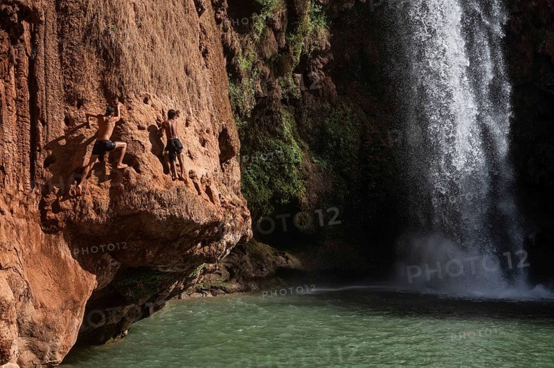OUZOUD, MOROCCO - OCTOBER 5, 2024: Two Moroccan boys climbs the rock before jump from into the water under a waterfall Ouzoud
