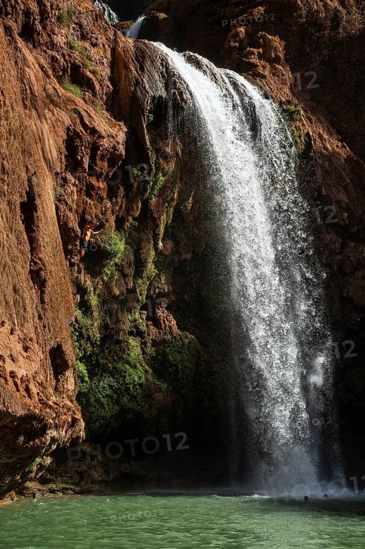Moroccan young man jumps from the high rock into the water under a waterfall Ouzoud