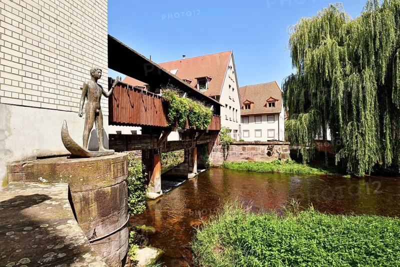 Ettlingen, Germany - August 13th 2025: Historic old town of Ettlingen Germany with wooden bridge over Alb river and sculpture of man holding fish