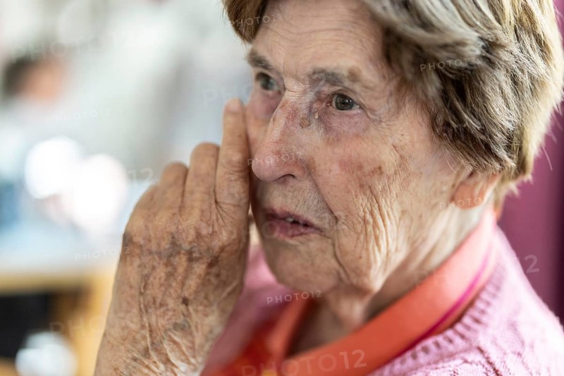 Close-up, authentic, unposed portrait of a 90+ year old senior woman with dementia and Alzheimer's disease in a retirement home, holding a hand to her face, Cologne, North Rhine-Westphalia, Germany