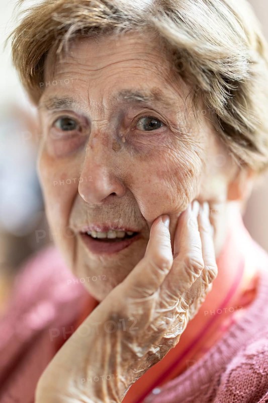 Close-up, authentic, unposed portrait of a 90+ year old senior woman with dementia and Alzheimer's disease in a retirement home, holding a hand to her face, Cologne, North Rhine-Westphalia, Germany