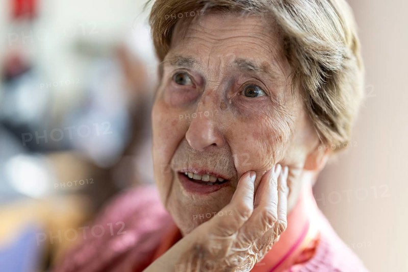 Close-up, authentic, unposed portrait of a 90+ year old senior woman with dementia and Alzheimer's disease in a retirement home, holding a hand to her face, Cologne, North Rhine-Westphalia, Germany