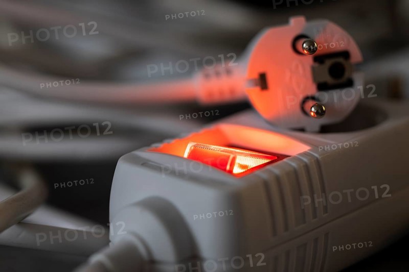 Close-up of a white power plug, Schuko plug, on a multiple socket with red indicator light, symbolic image for electricity, electrical energy, power consumption, studio shot, Germany
