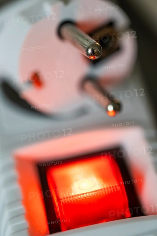 Close-up of a white power plug, Schuko plug, on a multiple socket with red indicator light, symbolic image for electricity, electrical energy, power consumption, studio shot, Germany
