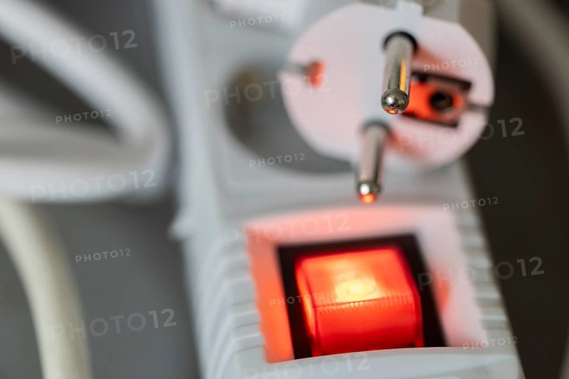 Close-up of a white power plug, Schuko plug, on a multiple socket with red indicator light, symbolic image for electricity, electrical energy, power consumption, studio shot, Germany