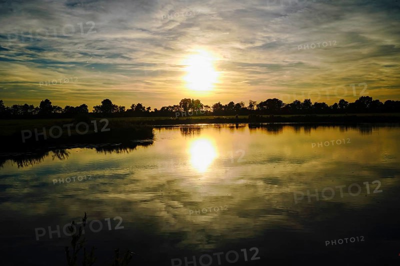 The setting sun paints the sky in warm colours that are reflected in the lake, natural landscape in Wüsting, 27798 Hude, Lower Saxony, Germany