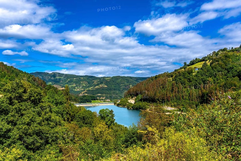 Serene ibiur reservoir nestled among lush hills of tolosa in the basque country, featuring a vibrant blue sky and fluffy white clouds, embodies natural tranquility