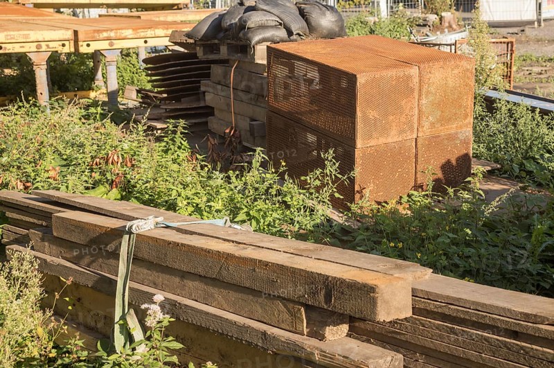 Borken, NRW, Germany, Various construction materials, including wooden planks and rusty metal crates, are stacked on the ground amidst weeds, awaiting use in a construction project