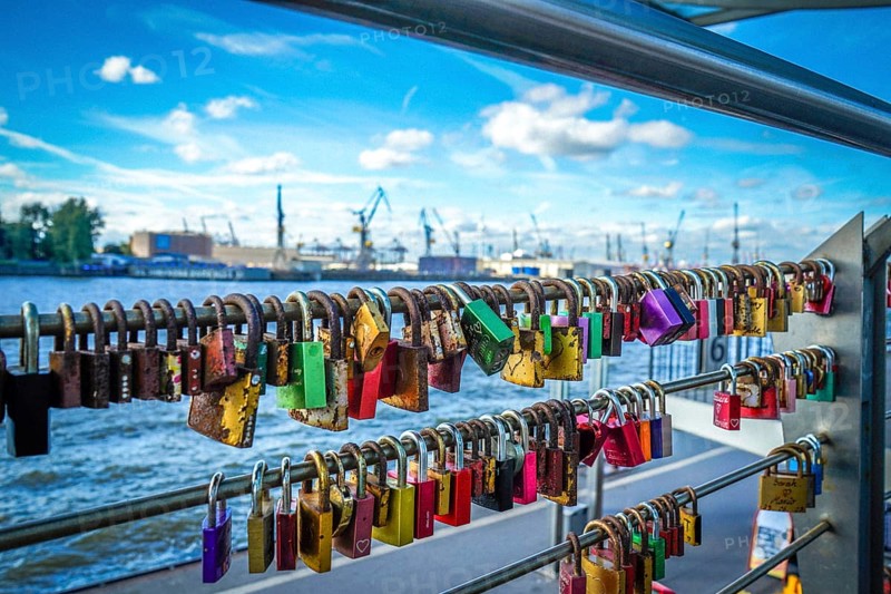 Many colourful love locks on a railing with a view of the harbour and cranes. View from the jetties in St. Pauli, 20359 Hamburg, Germany