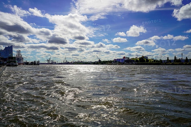 The Norderelbe with wavy water under a sunny sky, with urban background and silhouettes of cranes. View from the Landungsbrücken in St. Pauli, 20359 Hamburg, Germany