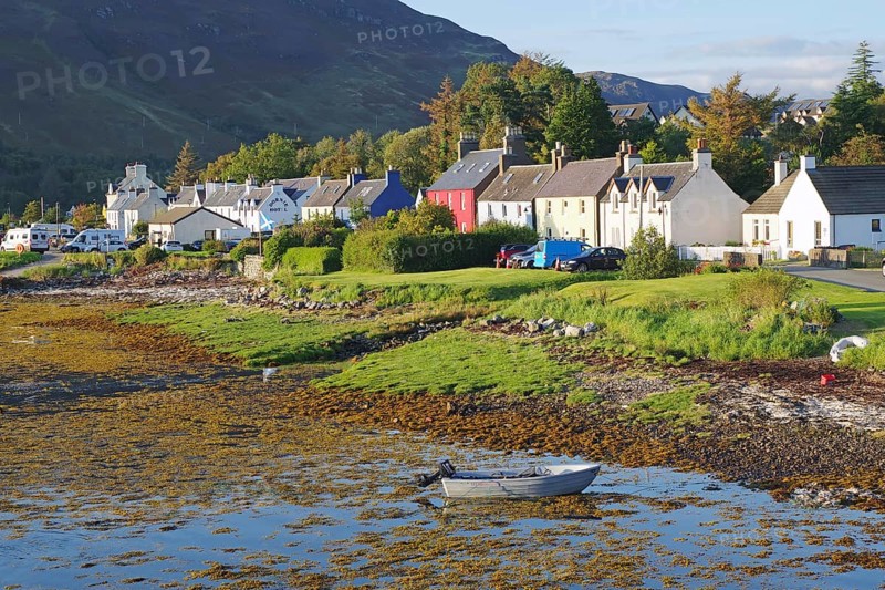 A quiet seaside village with colourful houses, a boat in the water and a green landscape against a mountain backdrop, Dornie, Scotland, United Kingdom