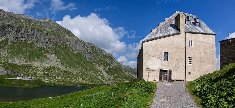 View to the right left side of the building of Ospizio Hospiz Herberge San Gottardo St. Gotthard built from 1230 in the 13th century with small entrance door main entrance to chapel Cappella di San Gottardo on top of Gotthard pass, left mountain lake Lago di Monti, Swiss Alps, Airolo, Canton Ticino, Ticino, Switzerland