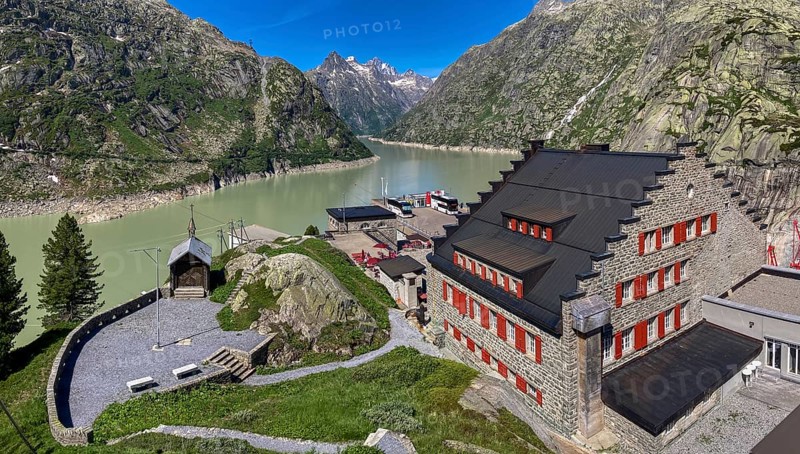 View from an elevated position to the right of the Grimselhospiz Hotel, built in 1932 on the Nollen, the first electrically heated hotel in Europe, on the left the Grimsel Hospiz mountain chapel, in the background Grimselsee, Guttanen, Canton of Bern, Switzerland
