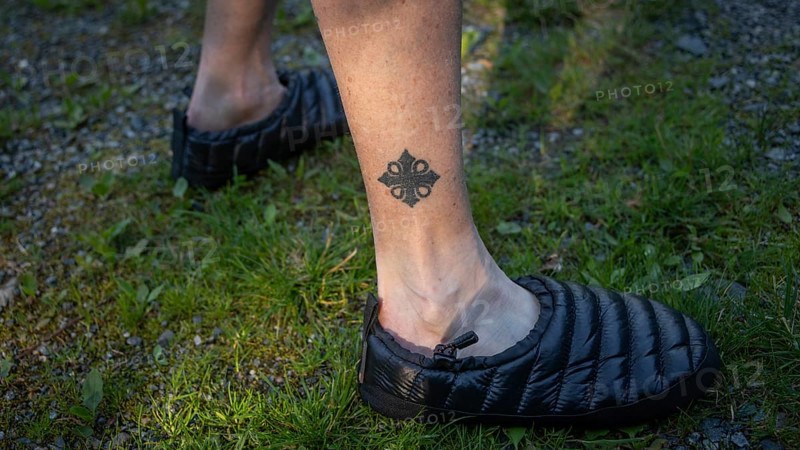Leg tattooed with Olav's cross, pilgrim in tap shoes on grassy ground, Olavsweg or Olavsleden, Norway