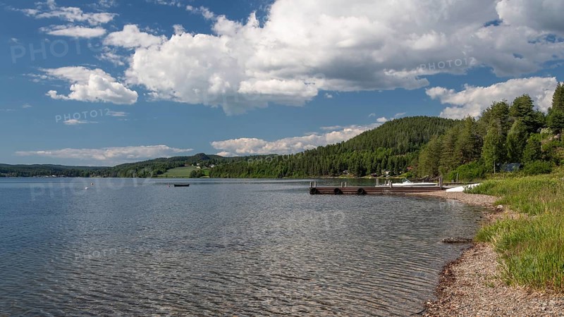 View of bathing area at Lake Mjøsa or Lake Mjosa with wooded shore under blue sky, Olavsweg or Olavsleden, near Tangen, Norway