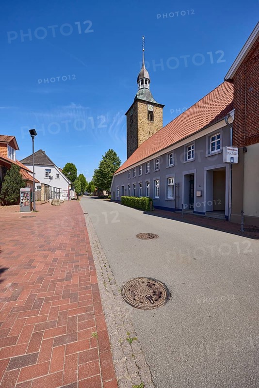 Streets, church tower of St. Johannis, historical buildings, pointed roof with red roof tiles, trees, clinker pavement, trees, blue sky, cirrostratus clouds, main street, Alfhausen, district of Osnabrück, Lower Saxony, Germany