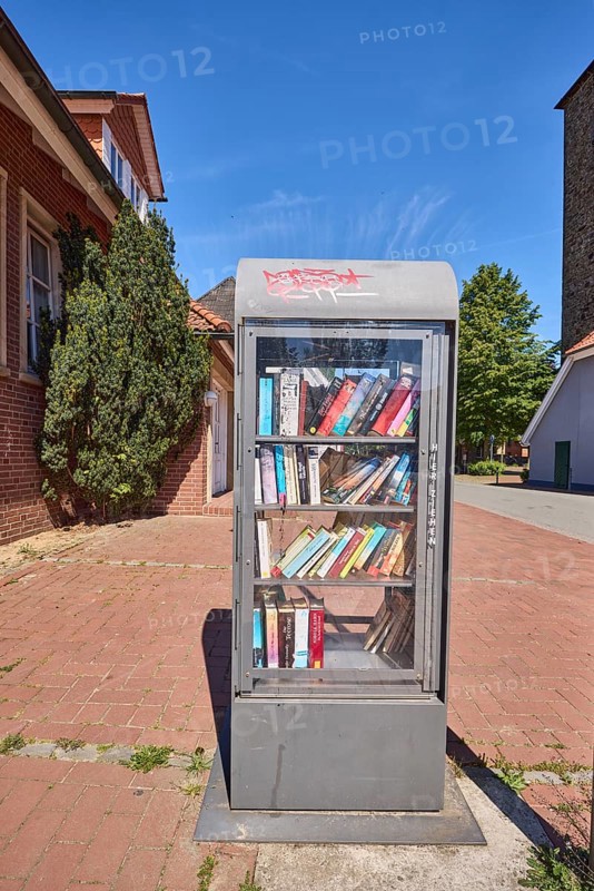 Book exchange box, street, general architecture, trees, clinker pavement, blue sky, cirrostratus clouds, main street, Alfhausen, district of Osnabrück, Lower Saxony, Germany