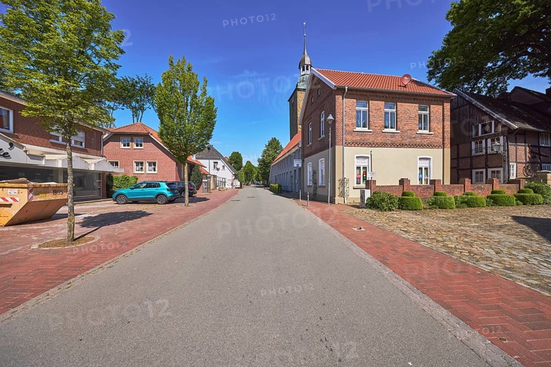 Street, church tower of St. Johannis, brick building, trees, blue sky, cirrostratus clouds, main street, Alfhausen, district of Osnabrück, Lower Saxony, Germany