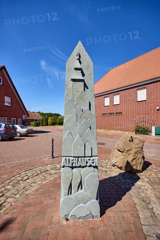 1000 year fountain, stone fountain, clinker brick building, pointed roof, clinker brick pavement, concrete paving stone road, blue sky, cirrostratus clouds, intersection of Hauptstraße with Nonnenpfad and In den Gärten, Alfhausen, district of Osnabrück, Lower Saxony, Germany