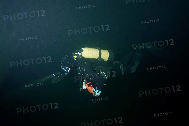 A diver in a diving suit explores a dark underwater environment. Dive site wreck of the Jura, Lake Constance, Bottighofen, Switzerland, Münsterlingen, Germany