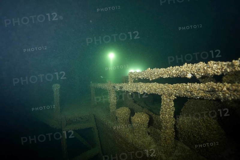A shipwreck covered with quagga triangle mussels (Dreissena rostriformis bugensis), an invasive species, is illuminated by rays of light in the darkness. Dive site wreck of the Jura, Lake Constance, Bottighofen, Switzerland, Münsterlingen, Germany