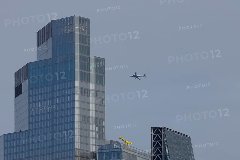 Jet passenger aircraft of British Airways airlines in flight in a blue sky with a city office block skyscraper building in the foreground, London, England, United Kingdom