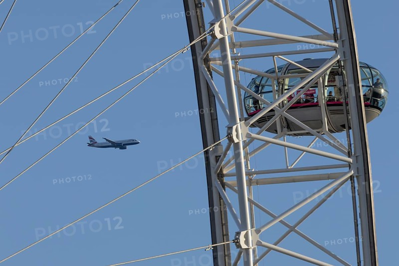 Airbus A320-232 jet passenger aircraft of British Airways airlines in flight in a blue sky with the London Eye wheel in the foreground, London, England, United Kingdom