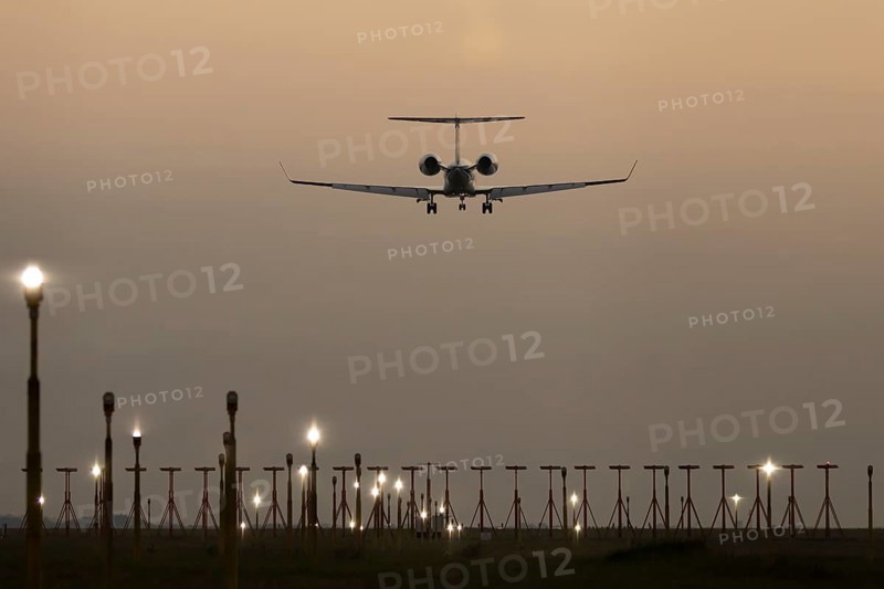 Executive business jet passenger aircraft landing over runway lights at sunset, London Stansted airport, Essex, England, United Kingdom