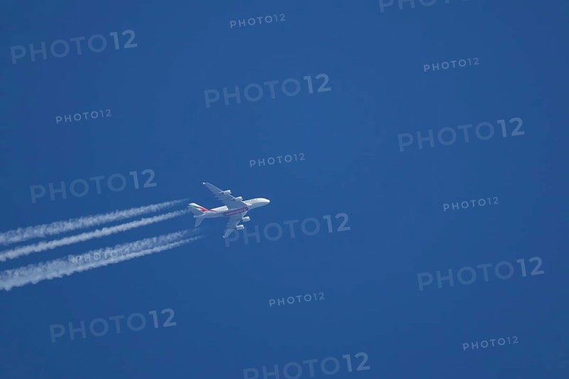 Airbus A380 jet passenger aircraft of Emirates airlines flying with vapour trails or contrails behind in a blue sky, England, United Kingdom