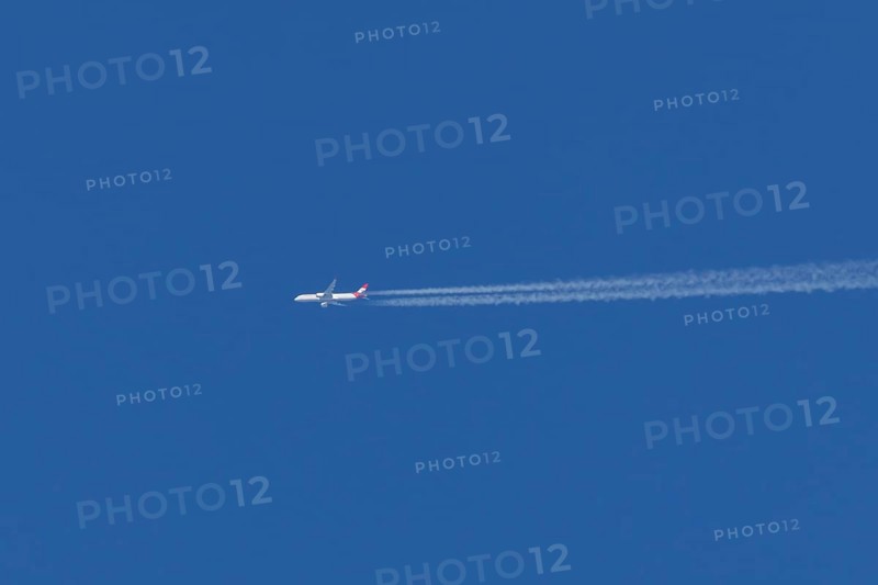 Airbus passenger jet aircraft of Austrian Airlines flying with a vapour trial or contrail behind in a blue sky, England, United Kingdom