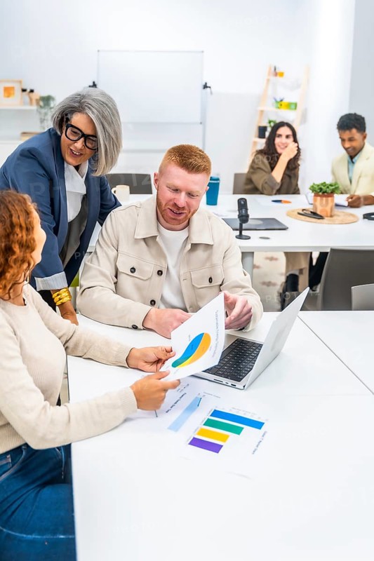 Business professionals collaborating and discussing marketing data with charts and graphs on documents and a laptop during a corporate meeting in a modern office