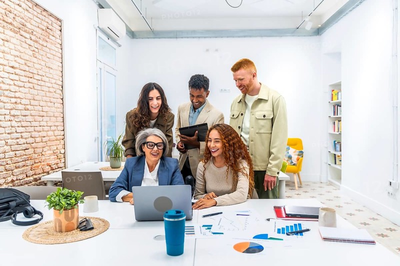 Diverse business team is collaborating and actively discussing financial data shown on a laptop screen, working together in a modern office environment