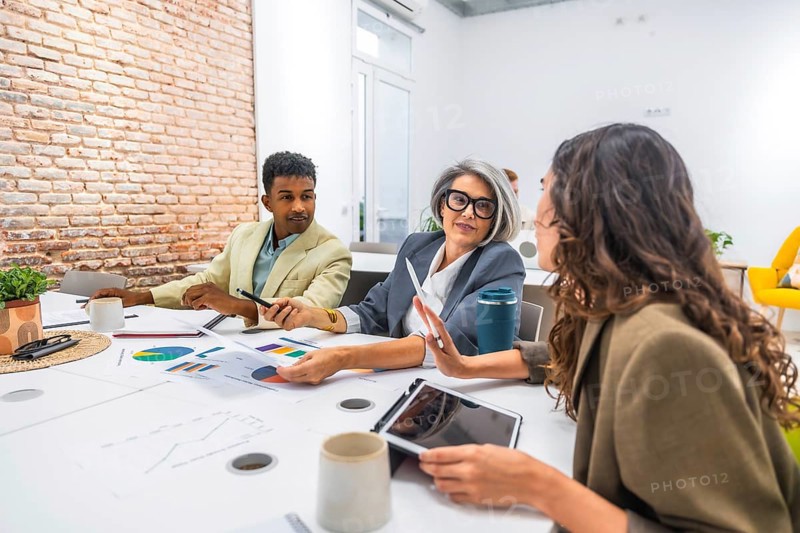Diverse business professionals collaborating in a modern office. Analyzing data and discussing financial charts during a productive team meeting. Demonstrating teamwork and professional communication