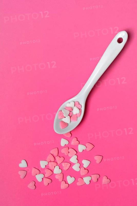 Sugar hearts with spoon on pink background
