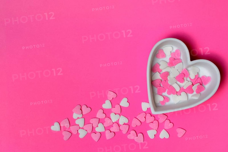 Sugar hearts in a heart-shaped bowl on a pink background