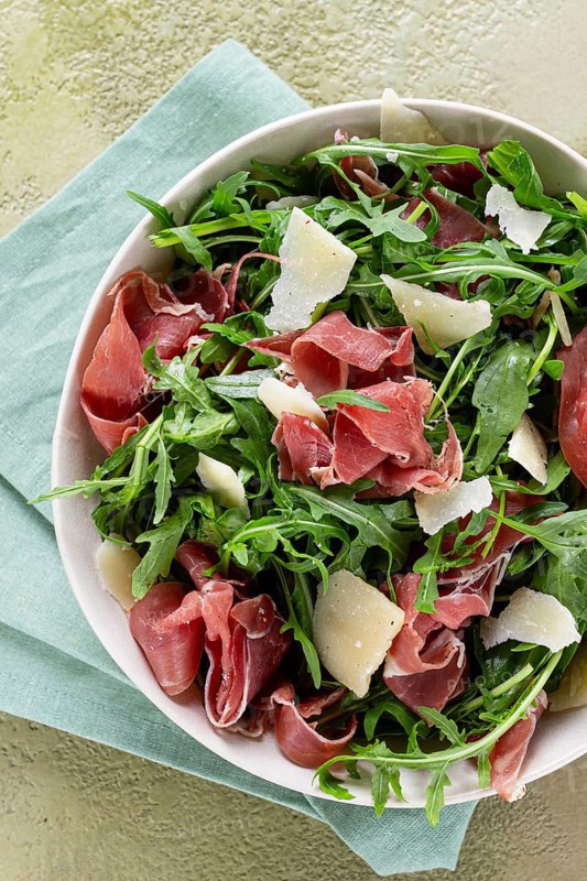 Fresh arugula salad with prosciutto and grated parmesan cheese, on a plate, homemade, no people