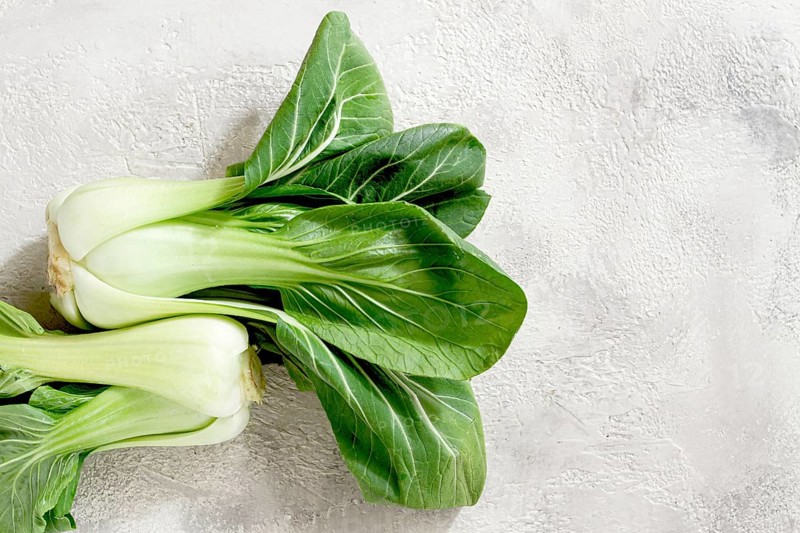 Fresh bok choy, laid out on a light gray surface, top view, natural light