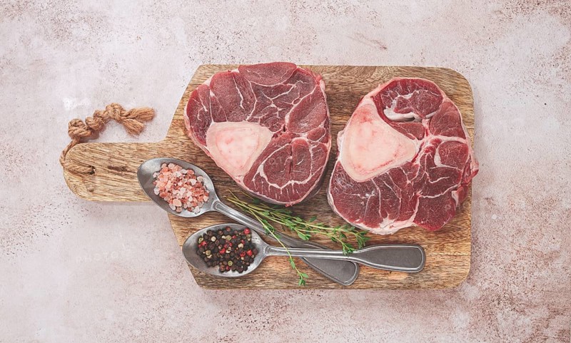 Knuckle on the bone, raw ossobuco meat, on a wooden chopping board, with spices, top view, no people