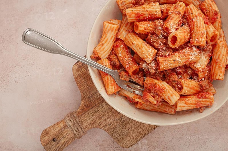 Rigatoni pasta with meat sauce and parmesan cheese on a light table, top view, homemade, no people