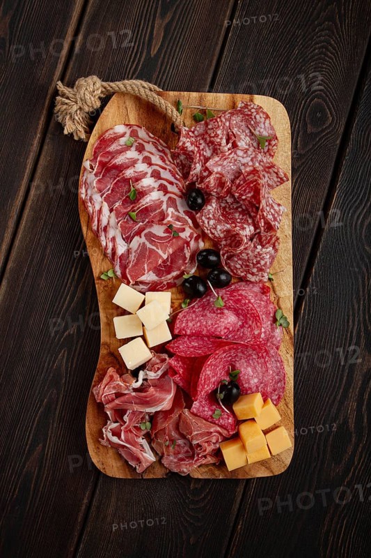 Assorted, sliced meat appetizer, prosciutto, salami and ham, with cheese and olives, on a wooden board, breakfast, top view, close-up, no people