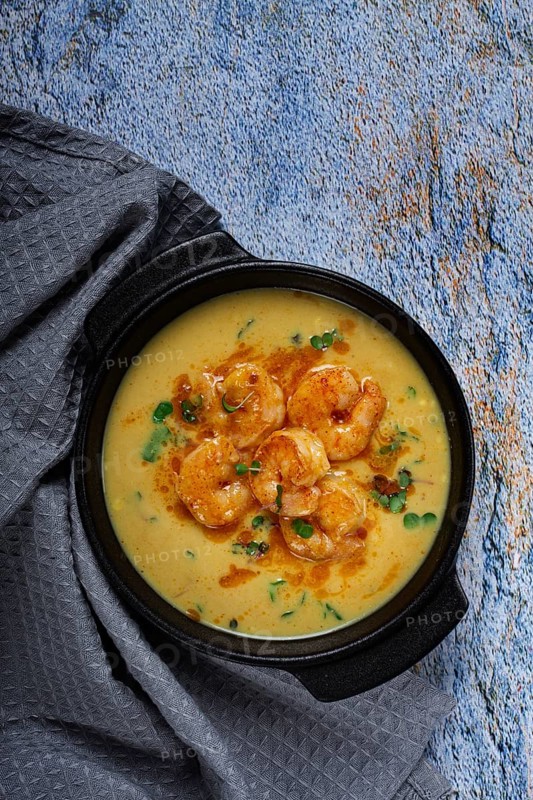 Creamy shrimp curry with spices, garnished with herbs, on a textured background, homemade, no people