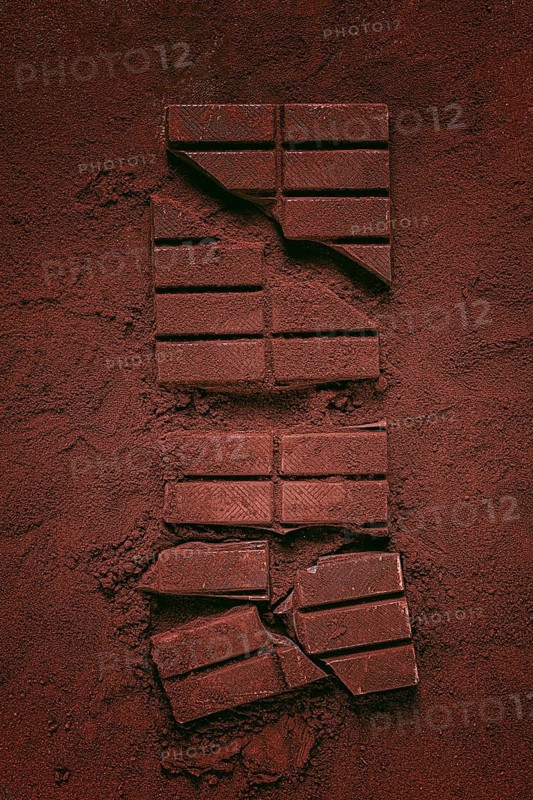 Chocolate bars broken and scattered on cocoa powder background with rich texture and color