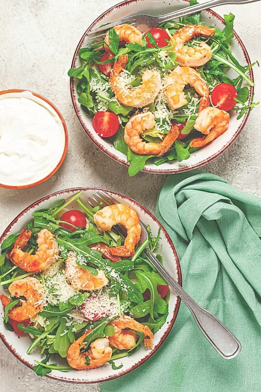 Two bowls of shrimp salad, arugula and cherry tomatoes, with parmesan cheese, healthy food
