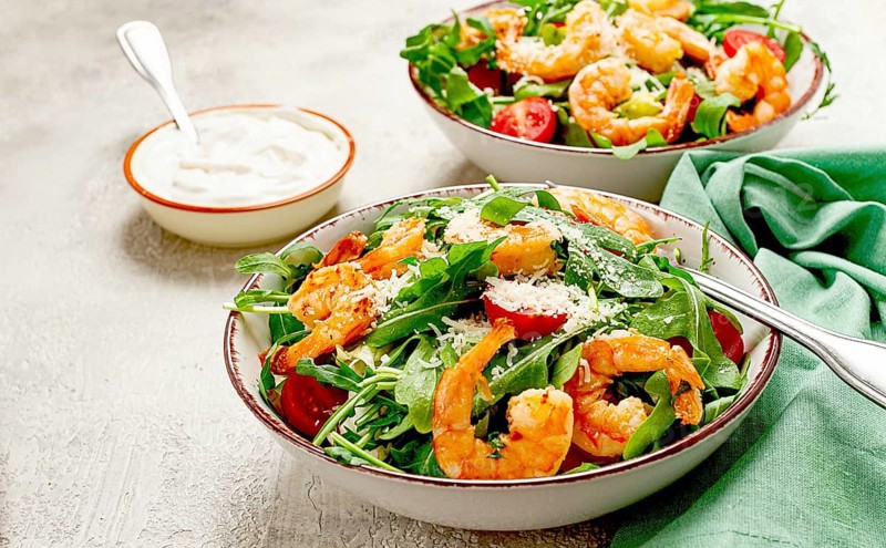 Two bowls of shrimp salad, arugula and cherry tomatoes, with parmesan cheese, healthy food