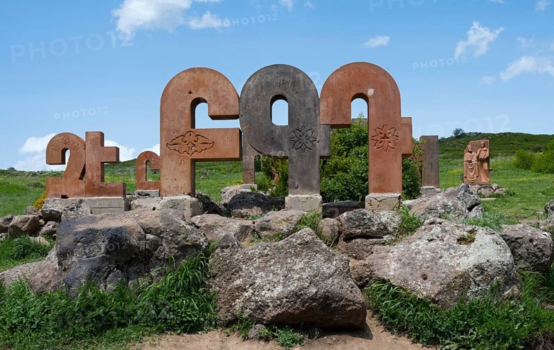 Stone pillars with traditional motifs, surrounded by large rocks and green grass, monument to the Armenian alphabet, Aparan, Aragazotn Province, Armenia