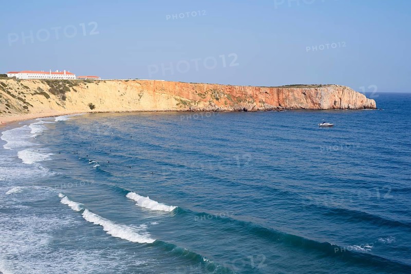 Cliffs with the Hotel Pousada de Sagres and surfers in the sea, Praia da Mareta, Sagres, Algarve, Portugal