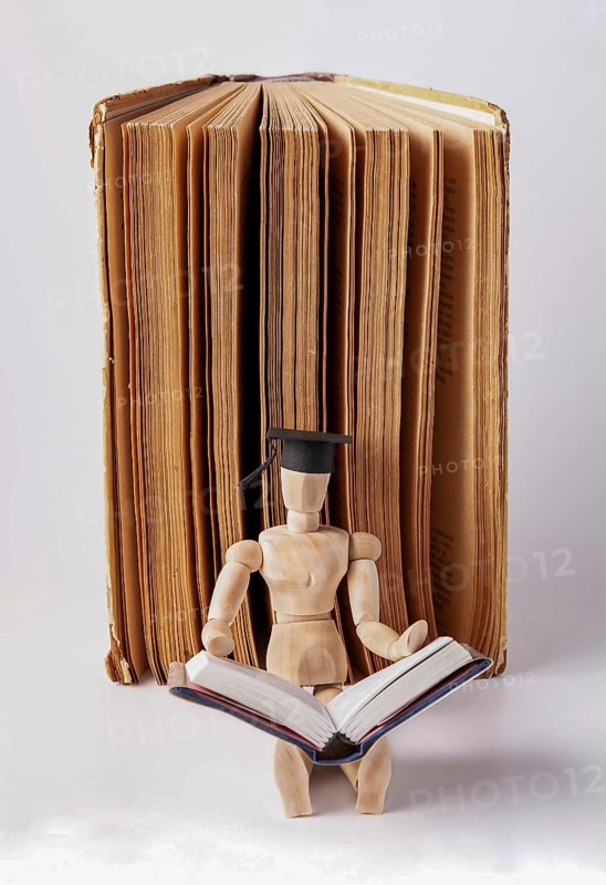 A wooden man in a student cap sits on the floor against the backdrop of an open book