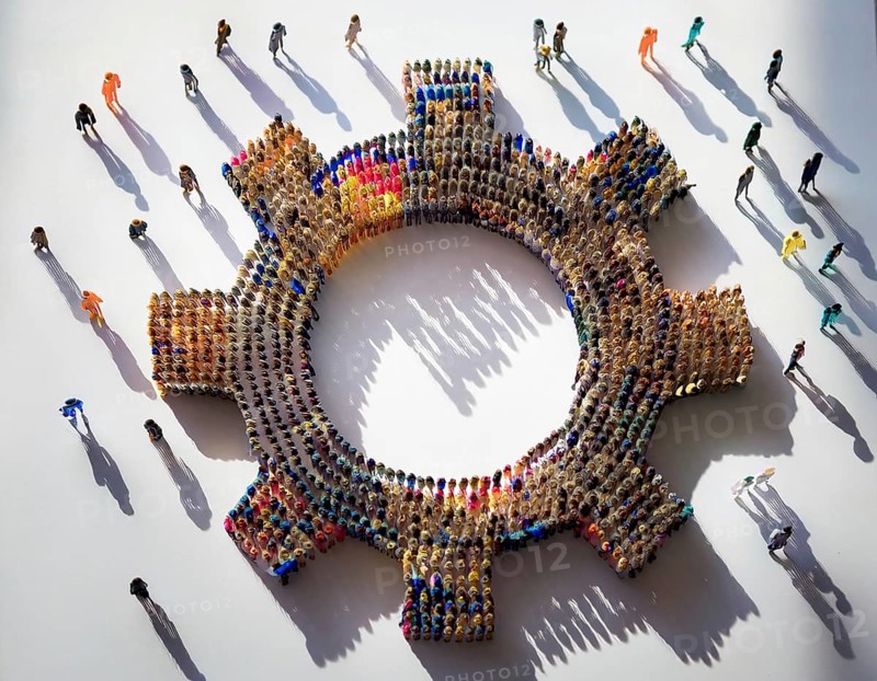 A diverse group of colorful individuals forms a gear shape, emphasizing collaboration, connection, and inclusivity highlighted by their distinct shadows on a white background, AI generated