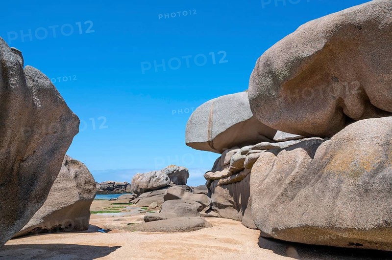 Spectacular pink granite rocks, sculpted by wind and sea, pile up on the beach of the Cote de Granit Rose, while the clear, turquoise-blue water reveals seaweed and light-coloured sand on the seabed at low tide, Tregastel, Cotes-d'Armor department, Brittany region, France