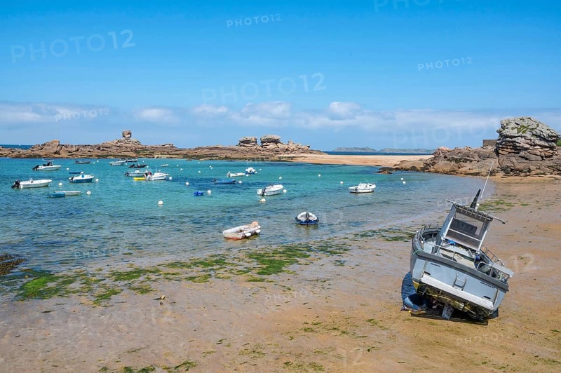 On the harbour beach of Tregastel on the Cote de Granit Rose, small boats lie on the light sand at low tide against the backdrop of the iconic pink granite rocks, Tregastel, Cotes-d'Armor department, Brittany region, France